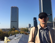 Na zdjęciu widać mężczyznę – Sławomira Strugarka, który stoi na dachu budynku, w tle widać panoramę Warszawy – w tym hotel Marriot.